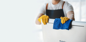 homem com luvas amarelas performando uma limpeza e higiene profissional em empresas ao limpar um computador