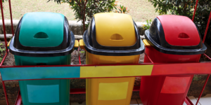 Três latas de lixo multicoloridas para coleta seletiva ao ar livre. As cores de cada caixa indicam o tipo de lixo a ser armazenado.